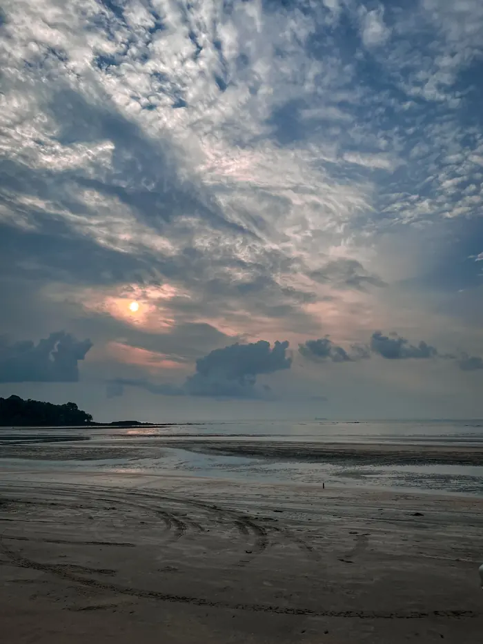 Sunlight breaking through cloud over a wide beach at low tide